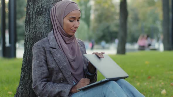 Tired Girl Student in Hijab Young Business Woman with Laptop Sitting in Park Near Tree on Green Lawn