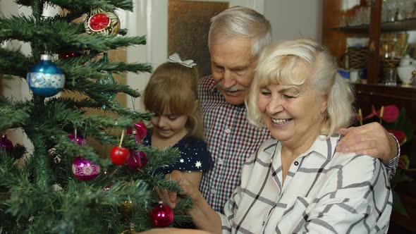 Children Girl with Elderly Couple Grandparents Decorating Artificial Christmas Pine Tree at Home