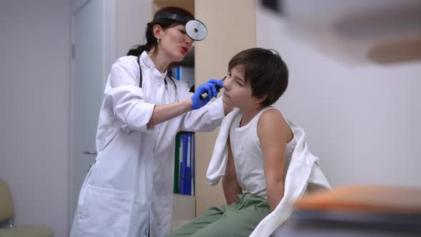 Caucasian Boy Sitting on Examination Couch As Smiling Doctor Checking Ears with Otoscope