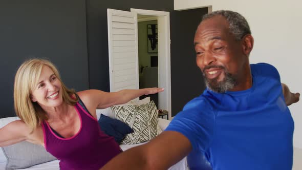 Diverse senior couple exercising together at home smiling and stretching