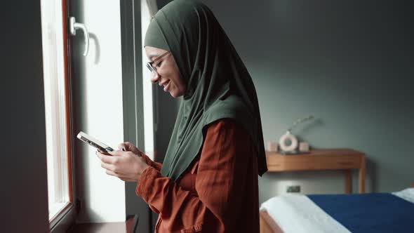 Positive Muslim woman wearing eyeglasses leafing tape by phone and looking at the camera