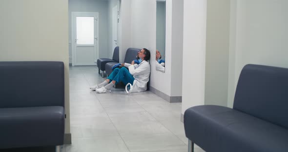 Exhausted Mature Doctor Sitting in Corridor of Medical Center