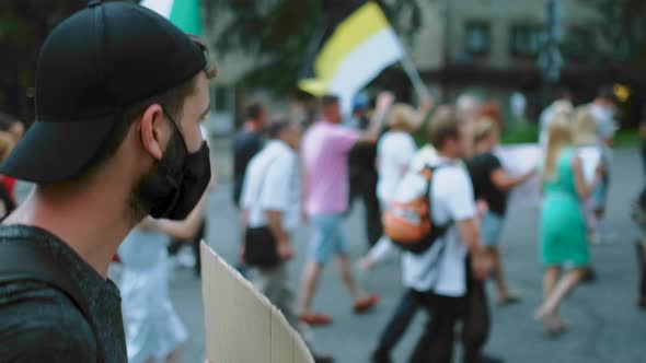 Male protester in coronavirus face mask in peaceful crowd with Russian flags.