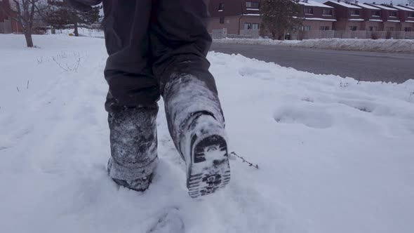 Young child walking in snow alongside road wearing grey snowpants boots gloves in winter