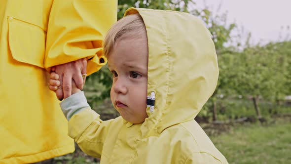 Portrait of Cute Baby Boy in Yellow Raincoat, Child Holds Mom's Hand. Love, Care, Attachment