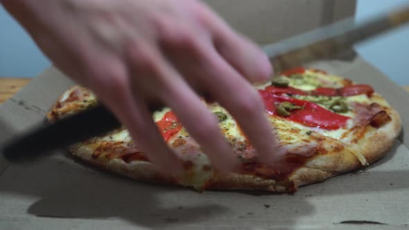 Male hands cutting a delicious pizza in slices with a knife inside the box.