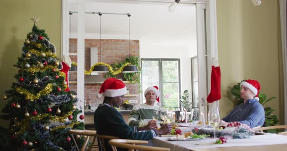 Happy group of diverse friends in santa hats celebrating meal at christmas time