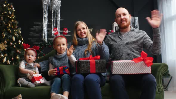 New Year - Family Sitting with Gifts on Their Knees and Wavws in the Camera