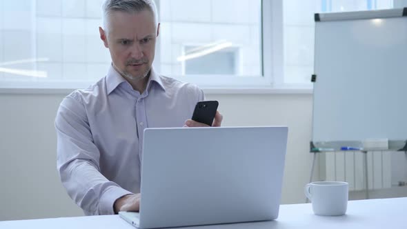 Middle Aged Businessman Using Smartphone at Workplace