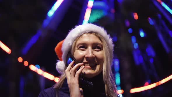 a woman chatting on her smartphone wearing a Santa hat is a night city.