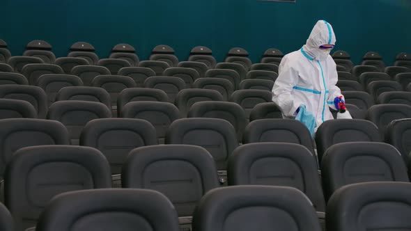 Worker in Protective Clothes Disinfecting Chairs at Cinema