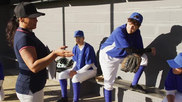 Diverse group of female baseball players and coach, coach instructing players on bench