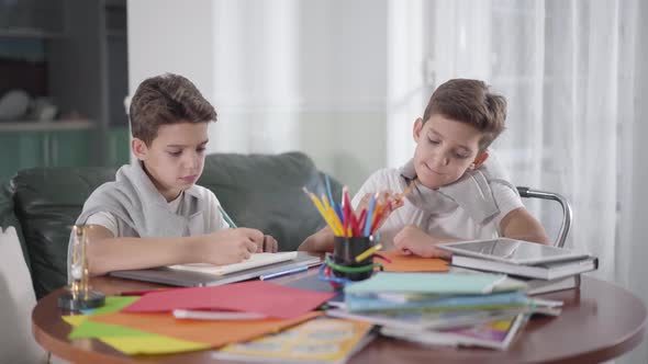 Two Creative Caucasian Twin Brothers Sitting at the Table and Drawing with Colorful Pencils