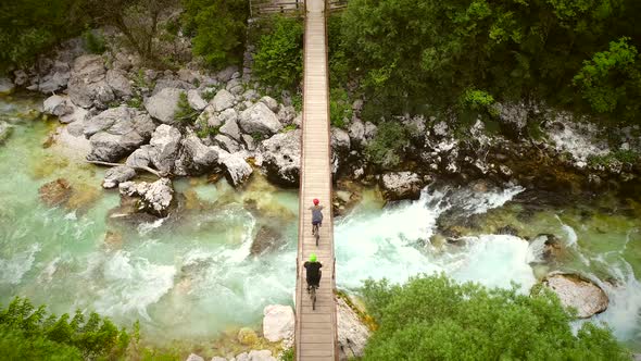 Aerial view of couple crossing a wooden bridge on bicycles at the Soca River.