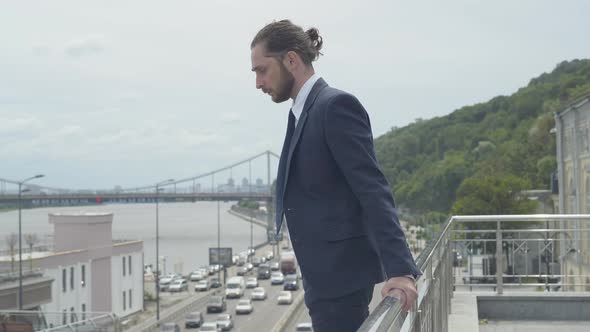 Side View of Suicidal Caucasian Businessman Standing at Bridge Fence with Cars Riding Along Highway