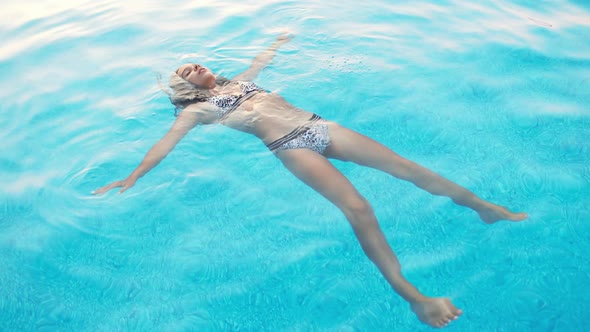 Girl in a in Leopard Swimsuit Swims in a Pool with Clear Water on Summer Vacation