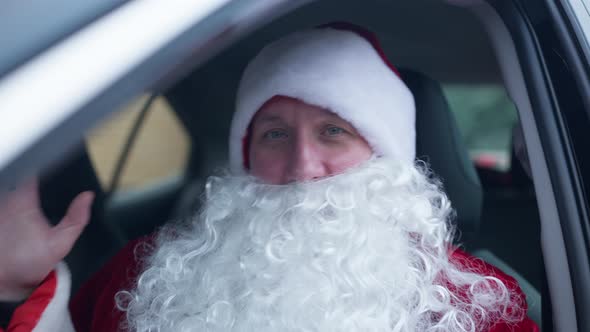 Santa Clause Waving Looking at Camera Sitting on Driver's Seat in Car