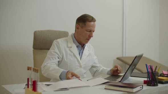 Confident Male Physician Examining Electrocardiogram of Patient and Typing Ecg Test Result on Laptop