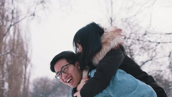 Young Man Giving Piggyback Ride To His Girlfriend in the Park on Snowy Winter Day