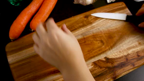 Woman's hands peeling fresh carrot above a wooden board close up