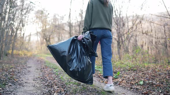 Pollution of Nature and the Environment. Female Legs, a Big Black Trash Bag