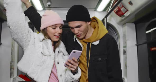 Cheerful Millennial Couple Looking at Smartphone While Going on Subway. Young Pretty Girl Holding