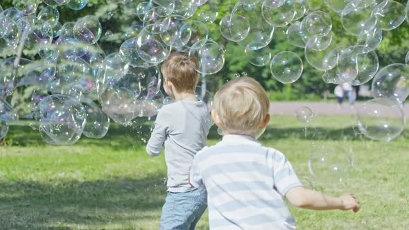 Boys Catching Giant Soap Bubble during Bubble Performance in Park