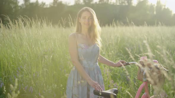 Portrait of Charming Young Woman Posing with Bicycle on Sunny Meadow. Young Smiling Caucasian Lady