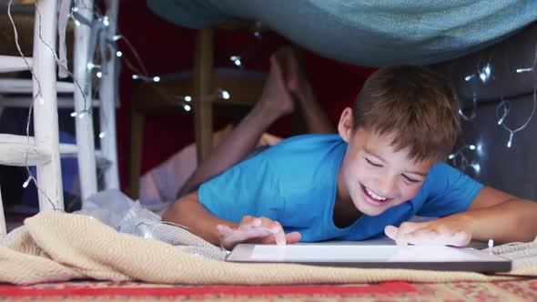 Caucasian boy smiling while using digital tablet under the blanket fort at home