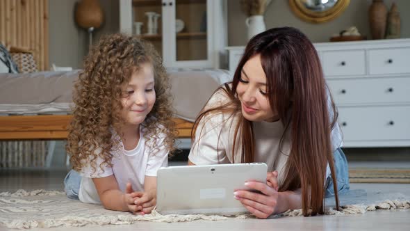 Brunette Mom and Kid Girl Play Online Game on White Tablet