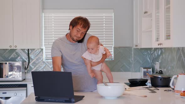 Father Holding Baby Infant and Using Computer Laptop at Home