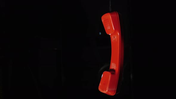 Red Telephone Receiver From a Retro Phone Hanging on a Wire on a Black Background