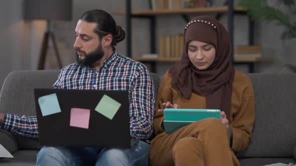 Serious Middle Eastern Couple Working Online in Home Office with Laptop and Tablet