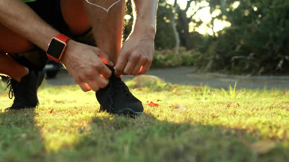 Man tying his shoe laces while jogging in park