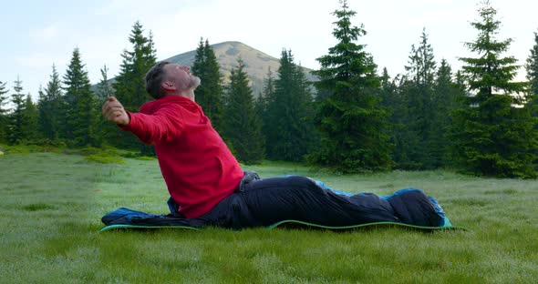 A Bearded Man in a Sleeping Bag Wakes Up in a Forest Glade in the Mountains