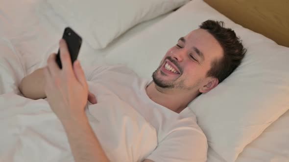 Young Man Doing Video Chat on Smartphone in Bed