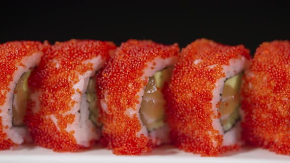 California Sushi Roll with Salmon Avocado Cucumber and Caviar on a White Plate on a Black Background