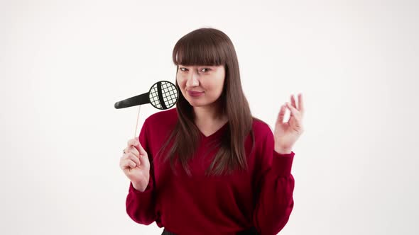 Young Beautiful Caucasian Darkhaired Woman Singing with Props Fake Microphone Over White Background