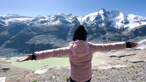 Back View of a Young Girl Embracing Fresh Air with Mountains Covered By Snow in Summer Season