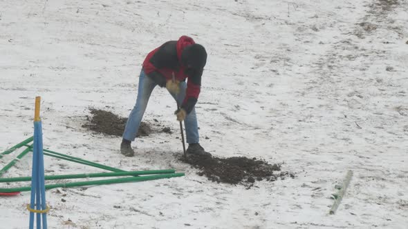 Man with Crowbar Make Holes in Frozen Ground