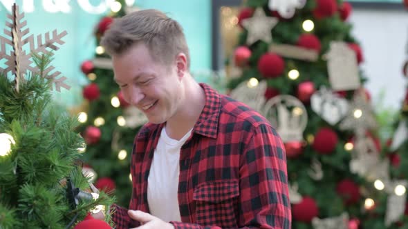 Young Happy Hipster Man Smiling While Looking At Christmas Trees Outdoors