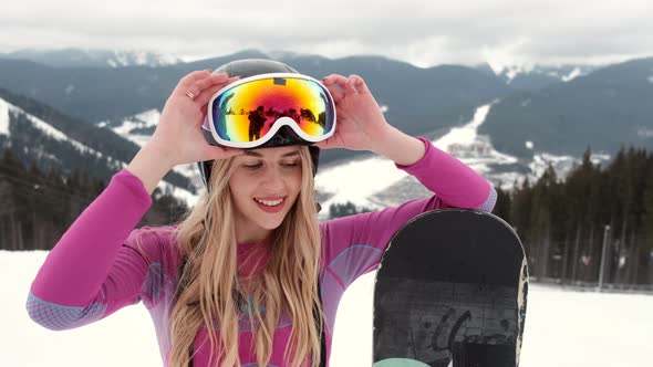 Young Girl Snowboarder is Smiling on the Top of the Mountain