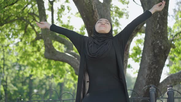 Portrait of Happy Young Muslim Woman in Black Traditional Clothes and Hijab Enjoying Sunny Summer