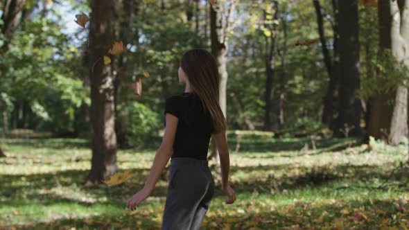 Girl Is Covering Her Face and Waving a Maple Tree Branch with Yellow Leaves in Autumn Park