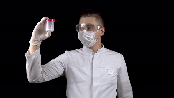 A Young Man Doctor Is Checking Sperm Tests. A Man Examines a Test Jar Containing Semen on a Black