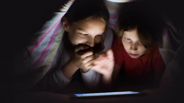 Girls Playing Online Game on Tablet While Hiding Under Blanket