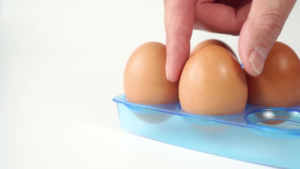 Hand takes one of the brown raw eggs on a blue plastic package