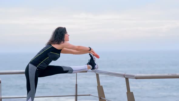 Active Woman Jogger on the Seashore Doing Stretching Exercises for Legs