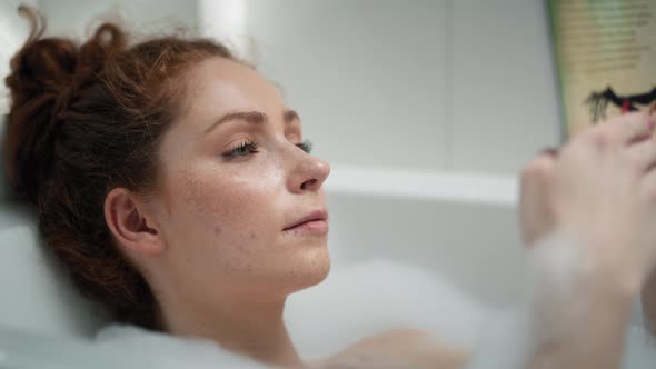 Caucasian redhead woman taking a bath and reading a book. Shot with RED helium camera in 4K.