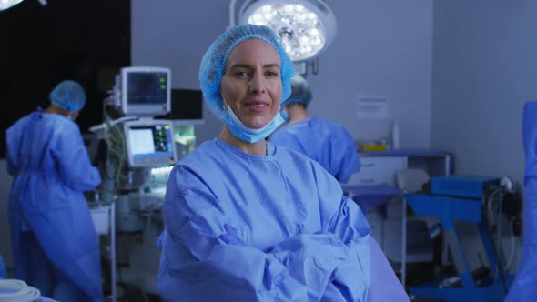 Portrait of caucasian female surgeon in lowered face mask smiling to camera in operating theatre